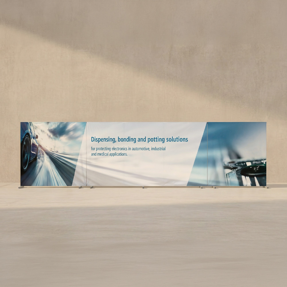 Ein mehrteiliger Bauzaunbanner mit links und rechts in einem blau-grauen Farbton. In der Mitte ist ein Text auf Englisch: "Dispensing, bonding and potting solutions. for protecting electronics in automotive, industrial an medical applications."