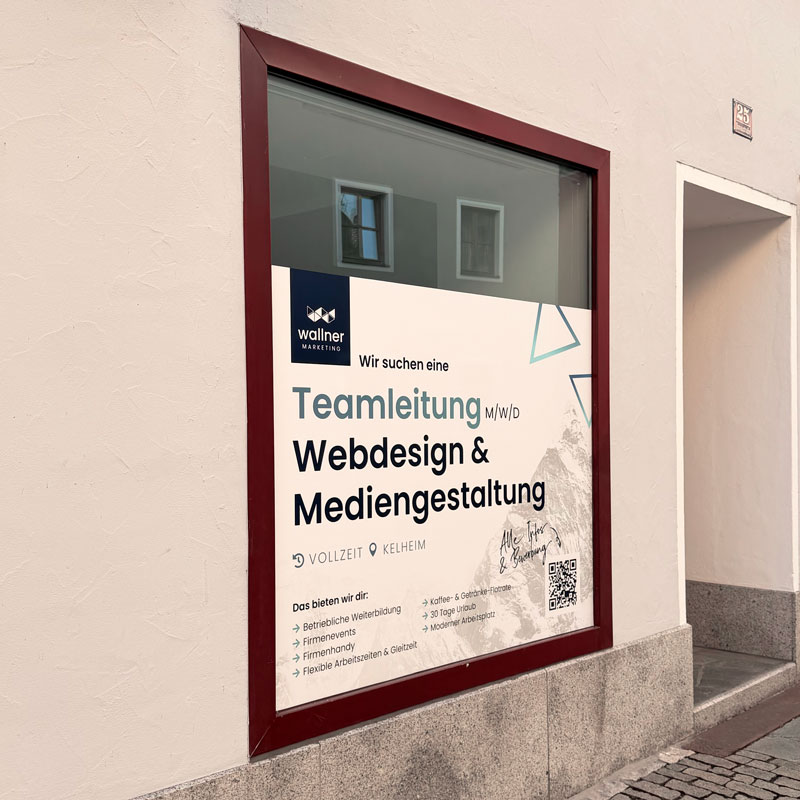 Ein weißes, blanko Nasenschild aus Metall befestigt an einem Gebäude mit roten Backsteinen und großen Glasfronten