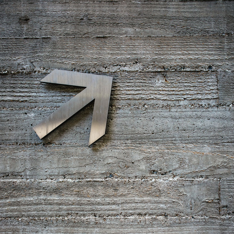 Eine Betonwand mit einem Pfeil aus Aluminium, der nach oben zeigt.
